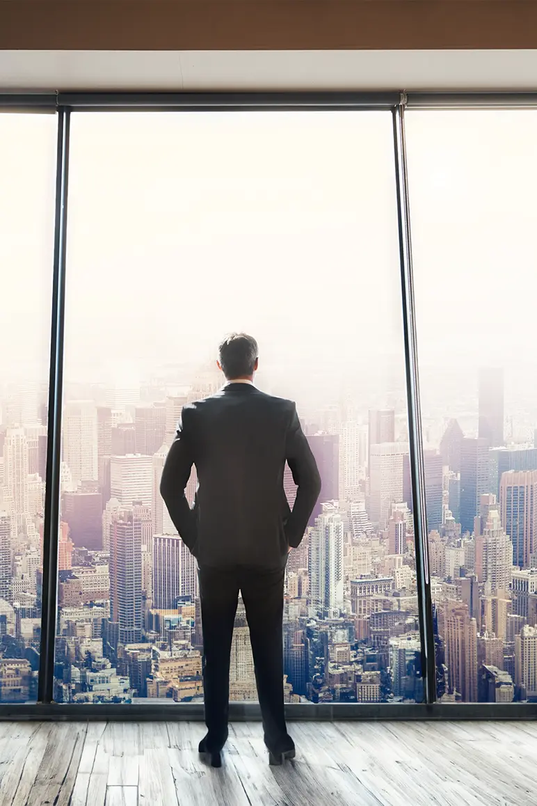 Man bij een raam met uitzicht op een drukke stad